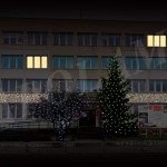 Budynek z oświetlonymi oknami i udekorowaną choinką - komponenty elektryczne i oświetlenie Polamp.